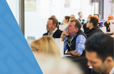 Construction safety professionals attending a HammerTech training session within the Australian construction industry, seated at tables and listening attentively during a workshop, with a blue branded overlay on the left side of the image.