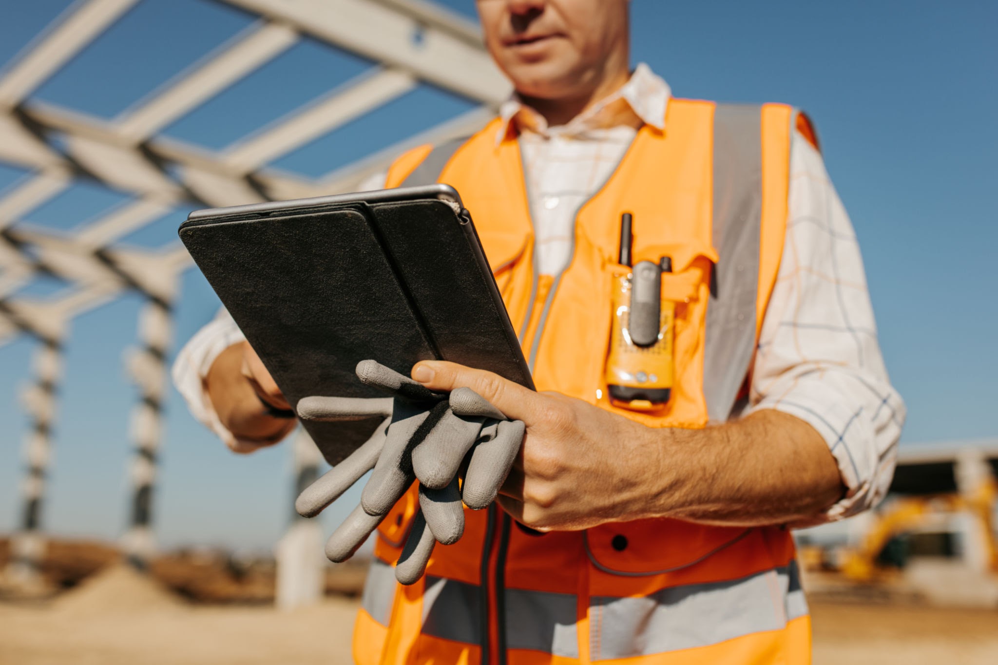 Construction safety software being used on a tablet on a construction site while wearing PPE and holding gloves
